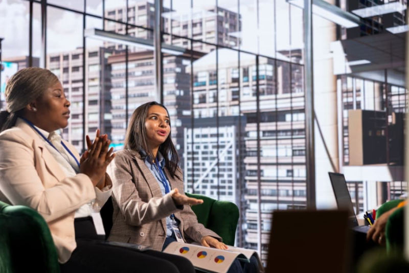 Two women business leaders meet with their team to discuss a project. 