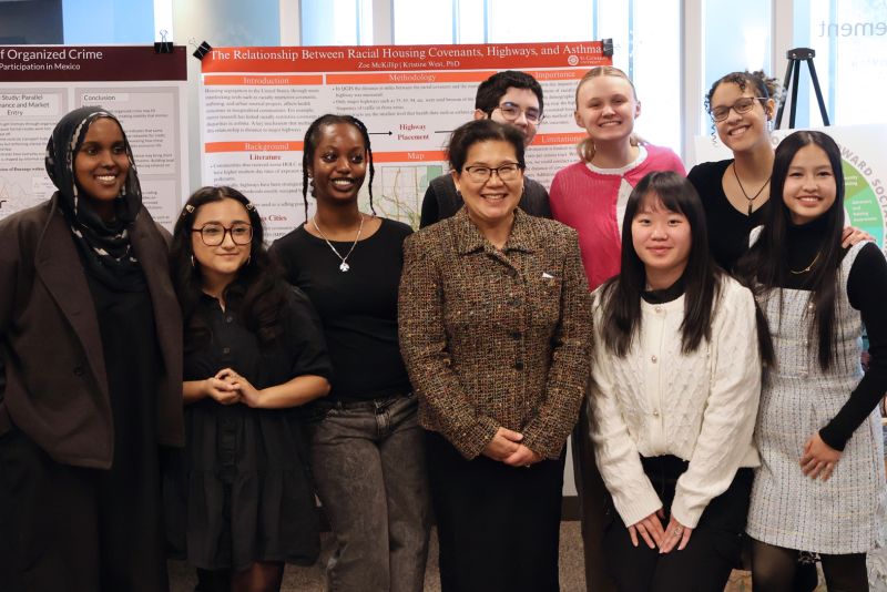 Mayor Her poses with a group of current students, standing in front of resarch boards.
