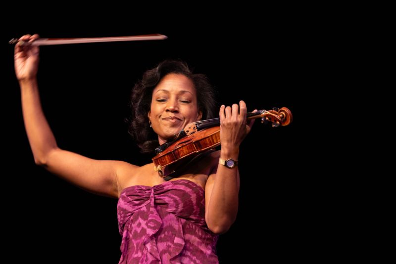 Close-up of Kelly Hall-Tompkins performing violin onstage in front of black background