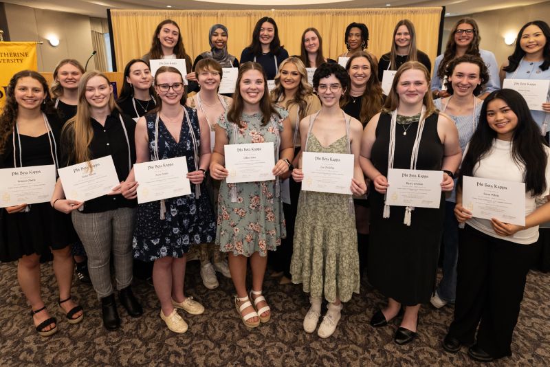 Phi Beta Kappa inductees stand holding their certificates. 