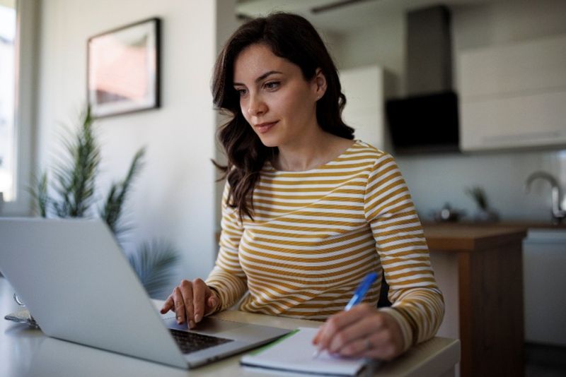 woman working at a computer holding a pen and taking notes