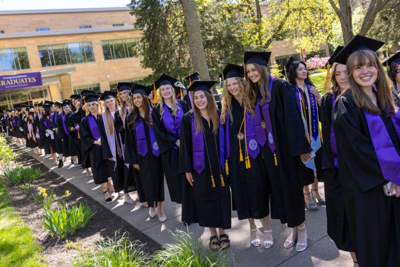 Graduates in caps and gowns line up outside for Commencement.
