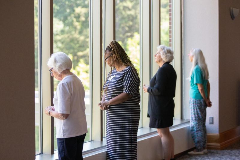 Four women stand looking out tall windows. 