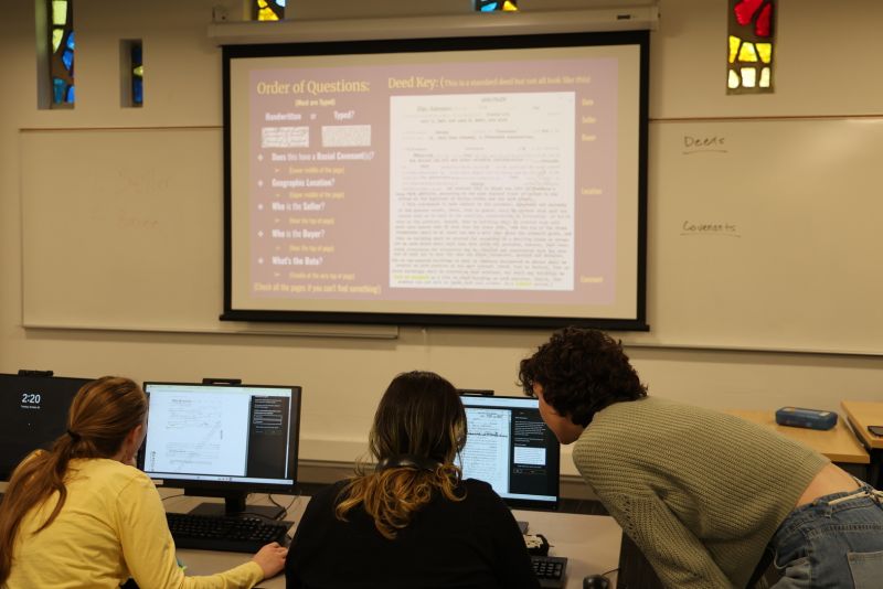 Students look over a laptop while doing research for a TRW class.