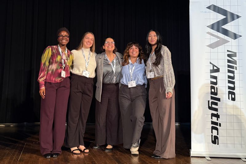 A group of four St. Kate's students and their supervisor gather on stage to celebrate a team win at the student data challenge by MinneAnalytics.