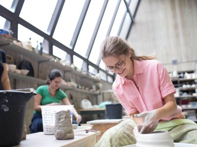 Student in the midst of building up a piece of clay pottery