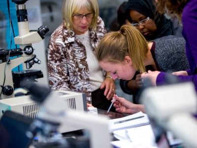 Student using eyedropper to populate microscope slide while professor and other students look on