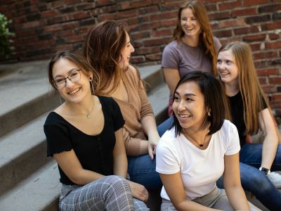 Five smiling women sitting on steps (of an auditorium?).