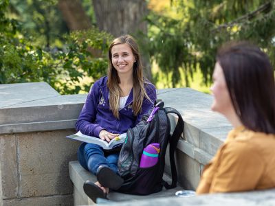 Two laughing students, studying outside on campus.