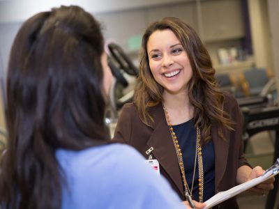 Student with an ID tag and a clipboard talking with someone (doing research?).