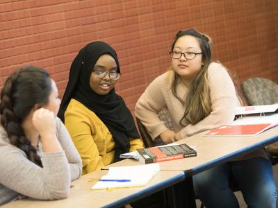 Three students studying together, with books and notes on the table in front of them.