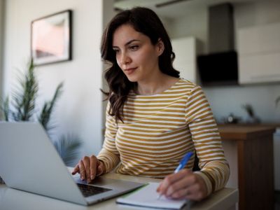 woman working at a computer holding a pen and taking notes
