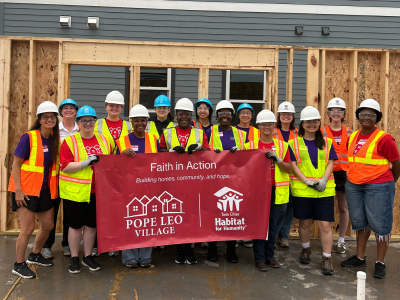 A group of people wearing neon safety vests and hard hats pose with a red banner at a construction site.