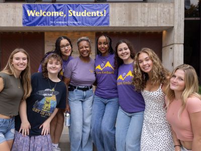 President Evans poses with a group of students in front a sign that reads "Welcome, Students!"