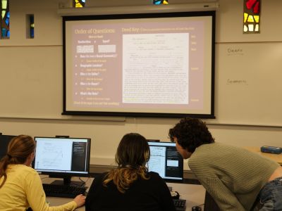 Students look over a laptop while doing research for a TRW class.