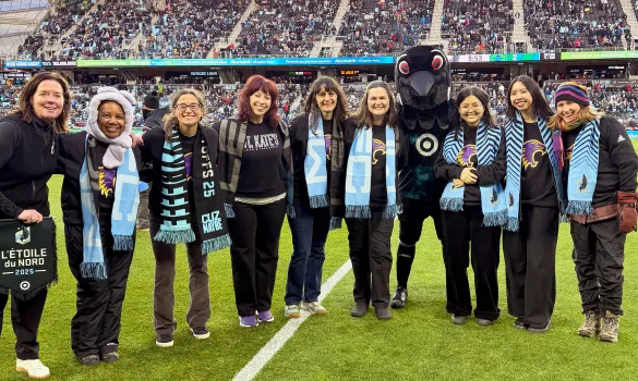 St. Kate's staff and students pose with the Loons mascot on the Minnesota United soccer field.