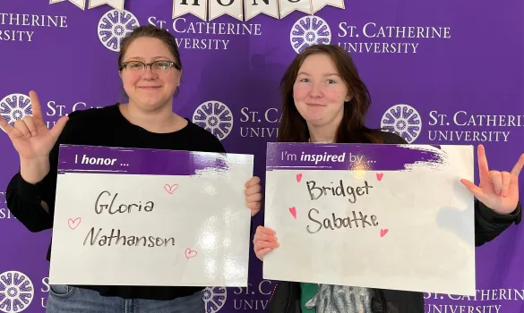 Two people standing in front of a purple backdrop each hold up whiteboards with names written on them. 