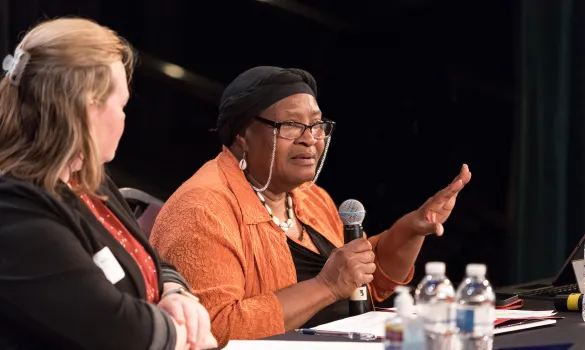 A woman sitting at a table speaks into a microphone.