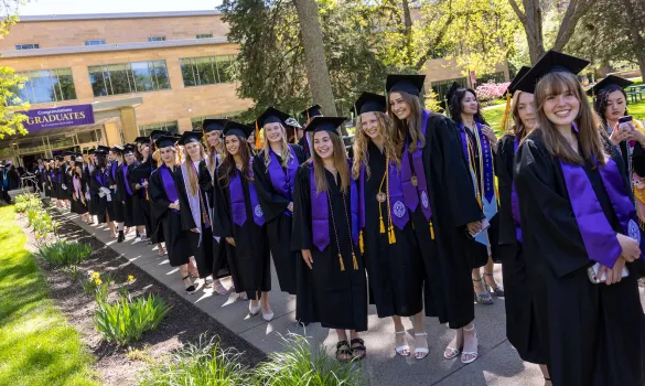 Graduates in caps and gowns line up outside for Commencement.