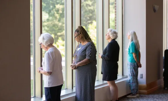 Four women stand looking out tall windows. 