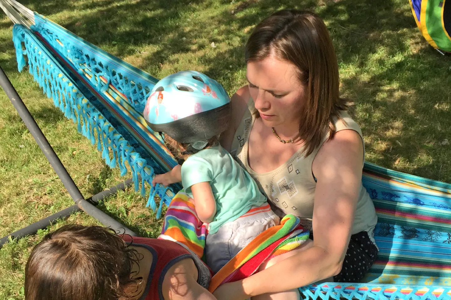 Alumna Jenica Domanico MAOT’12, founder of MOM plus ME, in hammock wearing green tank top, holding her two children.
