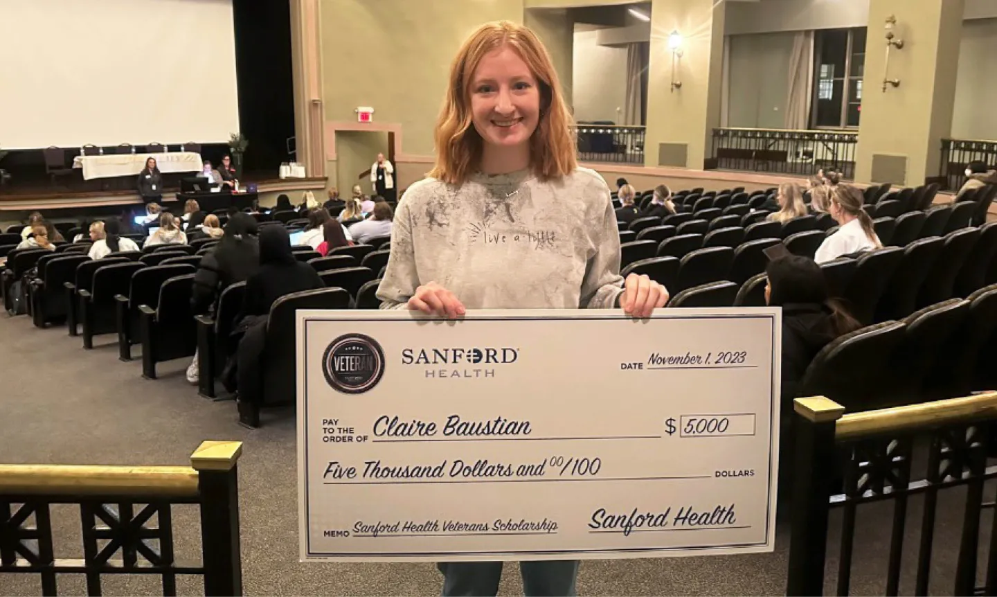 Student Claire Baustian holds a big $5,000 check from Sanford Health