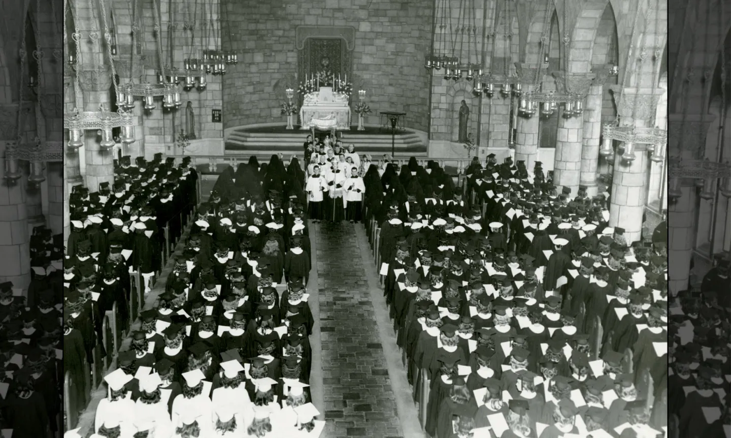 Black and white photo of students sitting in caps and gowns in Chapel pews.
