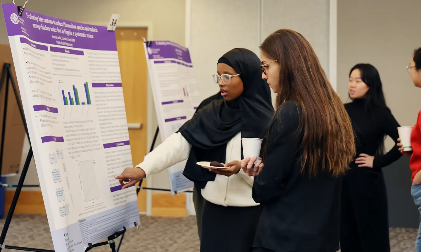 A student points at a poster presentation during the research week symposium.