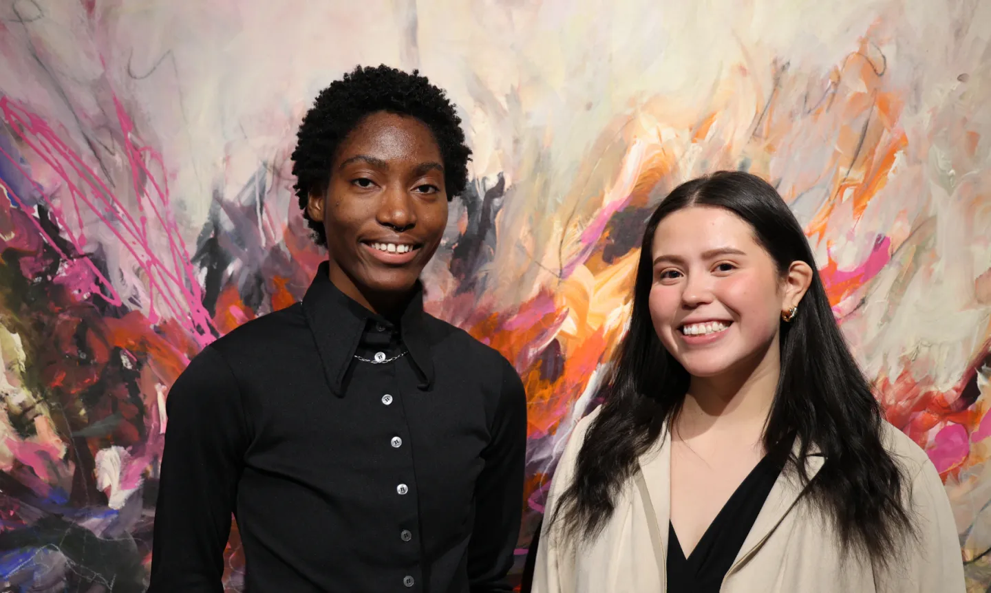 Burnices Barlue and Yasmin Leandro-Mendez stand and smile in front of a large painting.