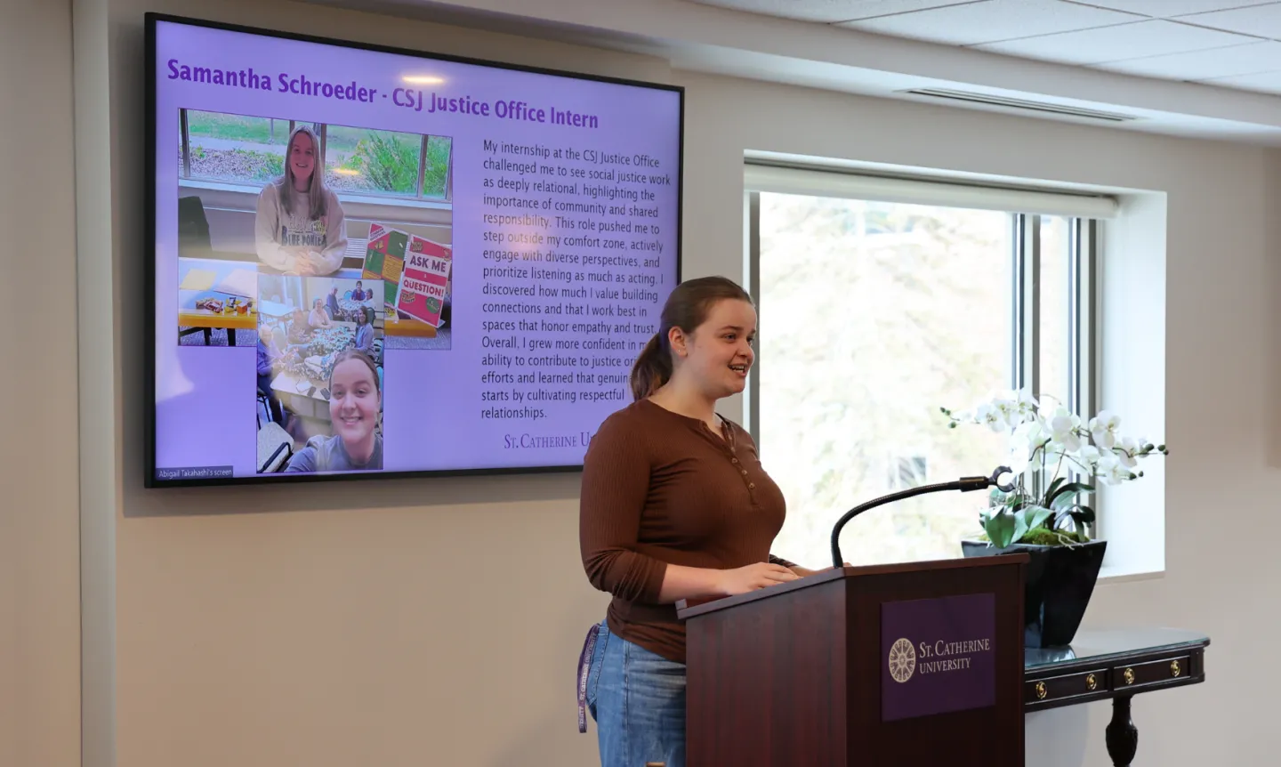 A student stands in front of a podium; behind her is a screen with a slide from a presentation.