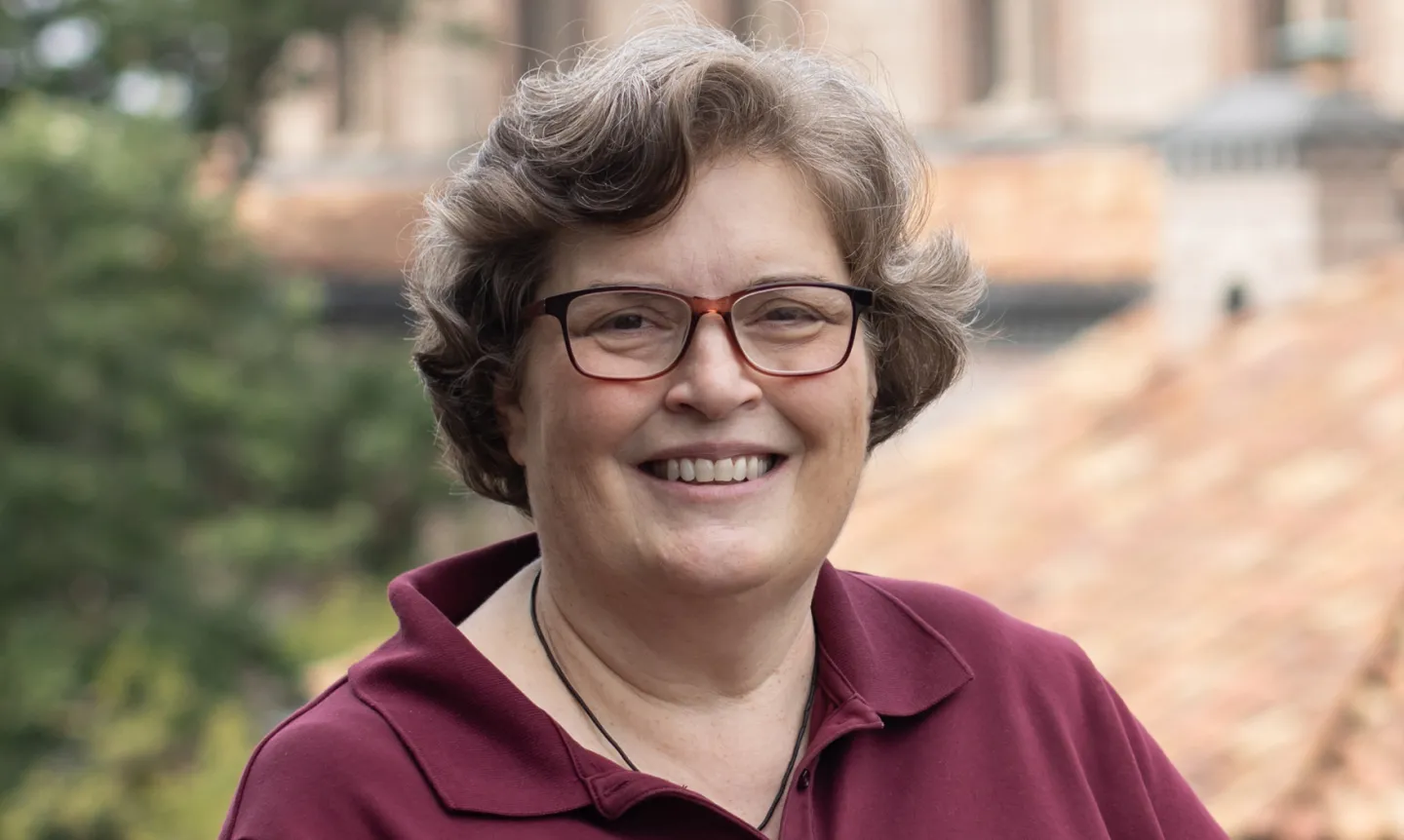 A photo of Jill Underdahl, CSJ, a woman with short hair and glasses wearing a maroon collared shirt.