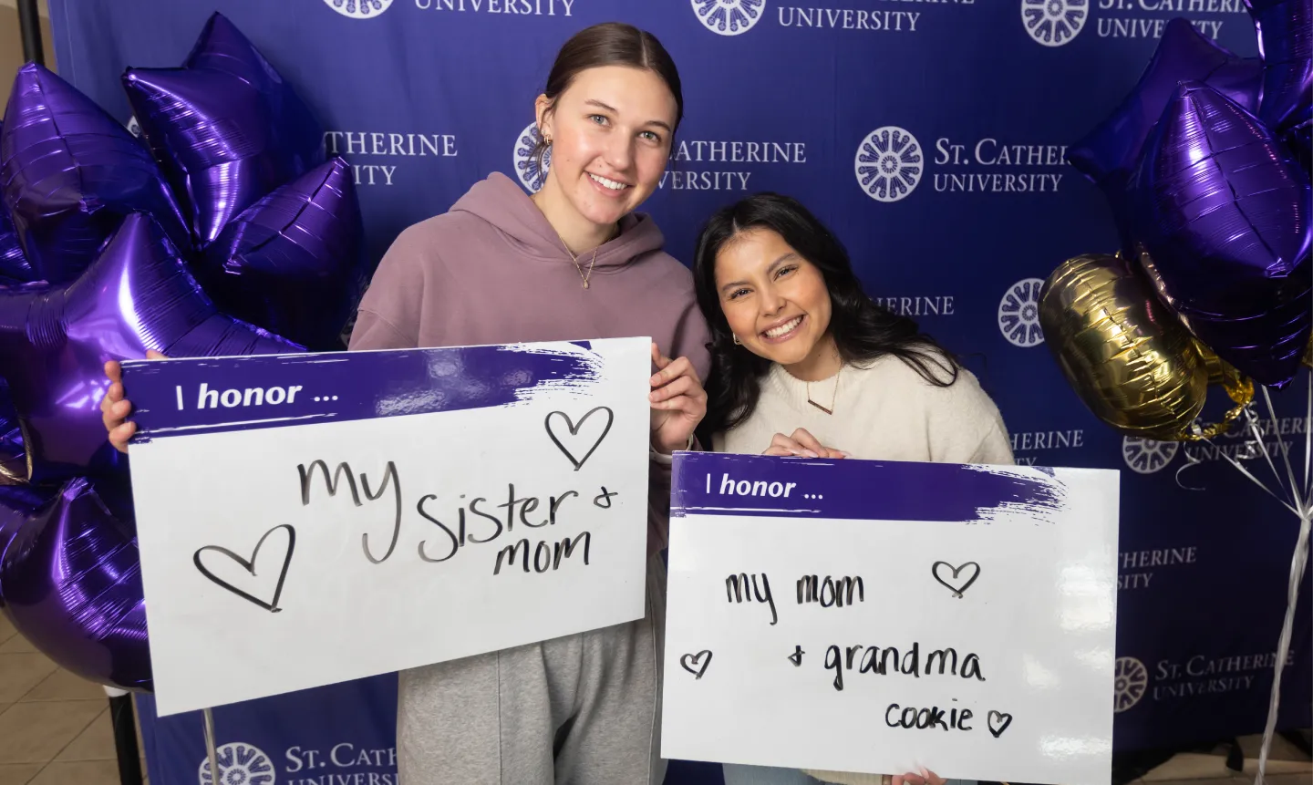 Two students hold up signs that say "I honor...my sister and mom" and "I honor...my mom and Grandma Cookie"