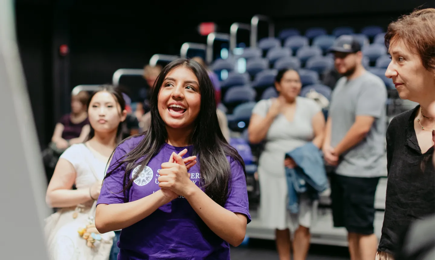 A student wearing a purple St. Kate's shirt looking at and talking about an out of frame poster presentation.