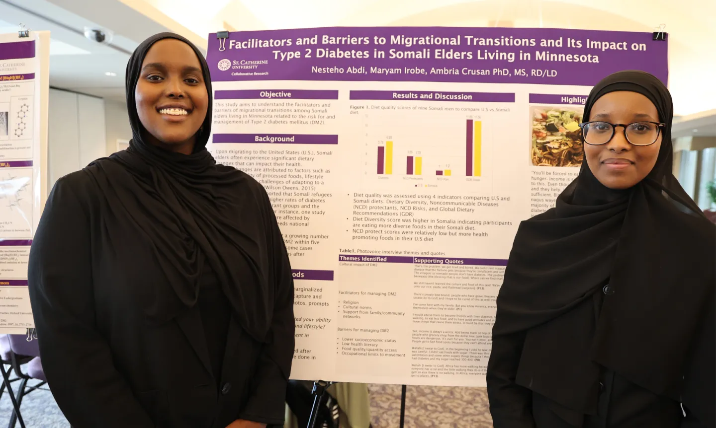 Two students, smiling and wearing black, stand in front of a poster with their research.