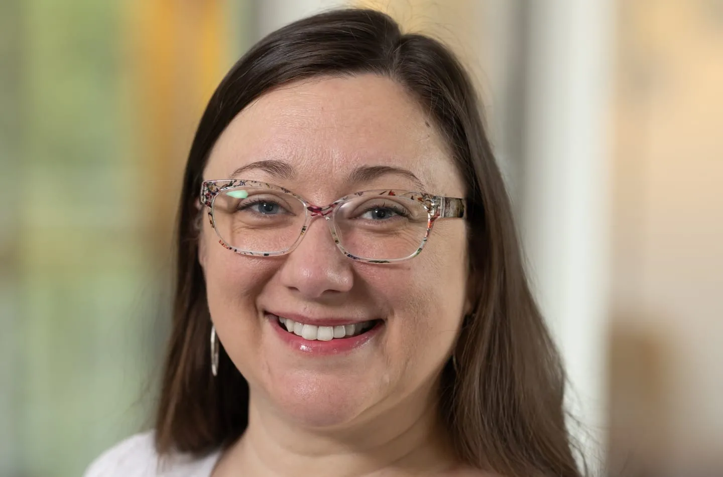 Person smiling while wearing patterned eyeglasses, with a blurred indoor background.