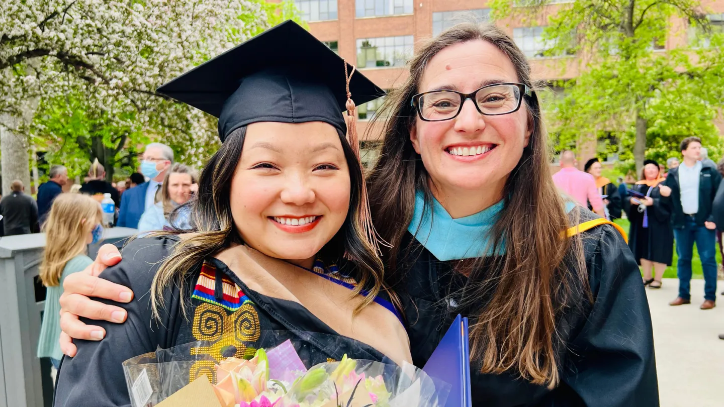 Two smiling women, one wearing a graduation cap and gown.