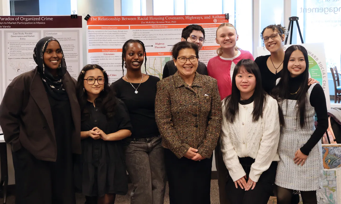 Mayor Her poses for a photo with a group of students, standing in front of research posters.