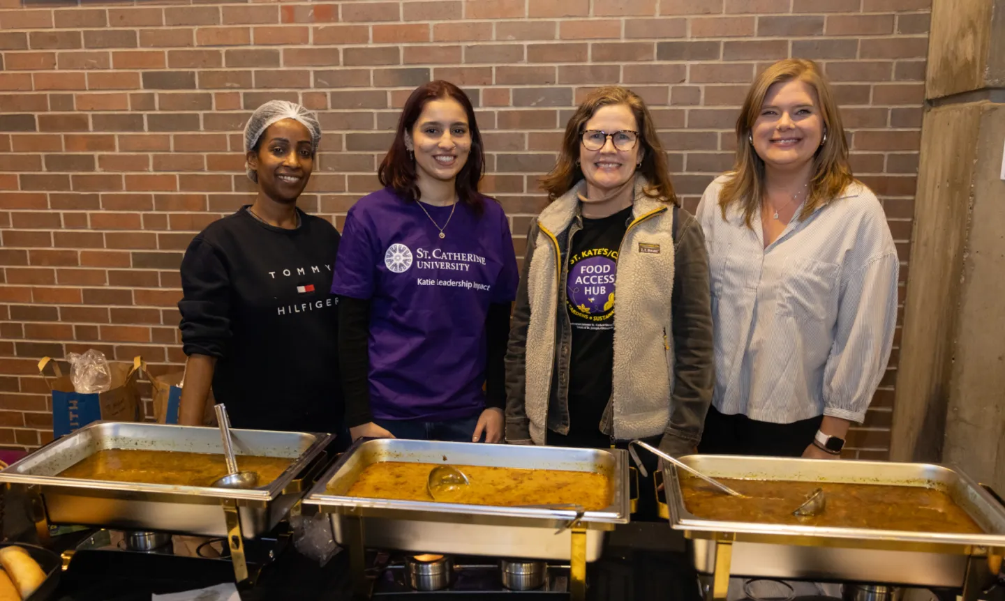 Four people stand behind a soup buffet table