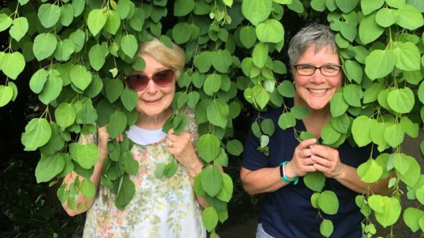 Two women stand and smile underneath a tree with branches hanging down
