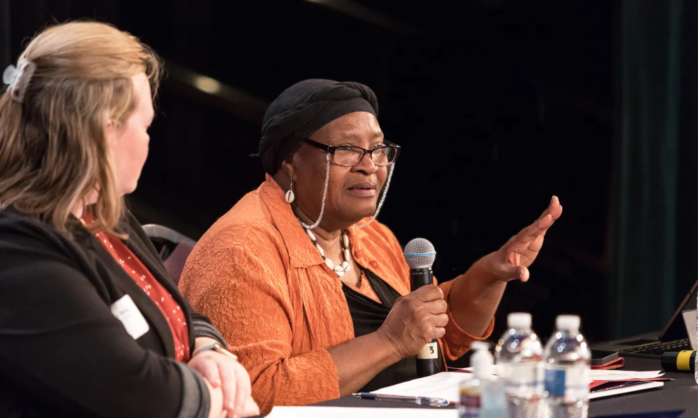A woman sitting at a table speaks into a microphone.