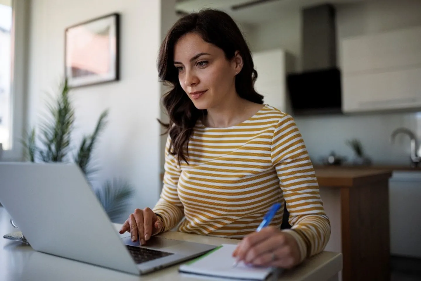 woman working at a computer holding a pen and taking notes