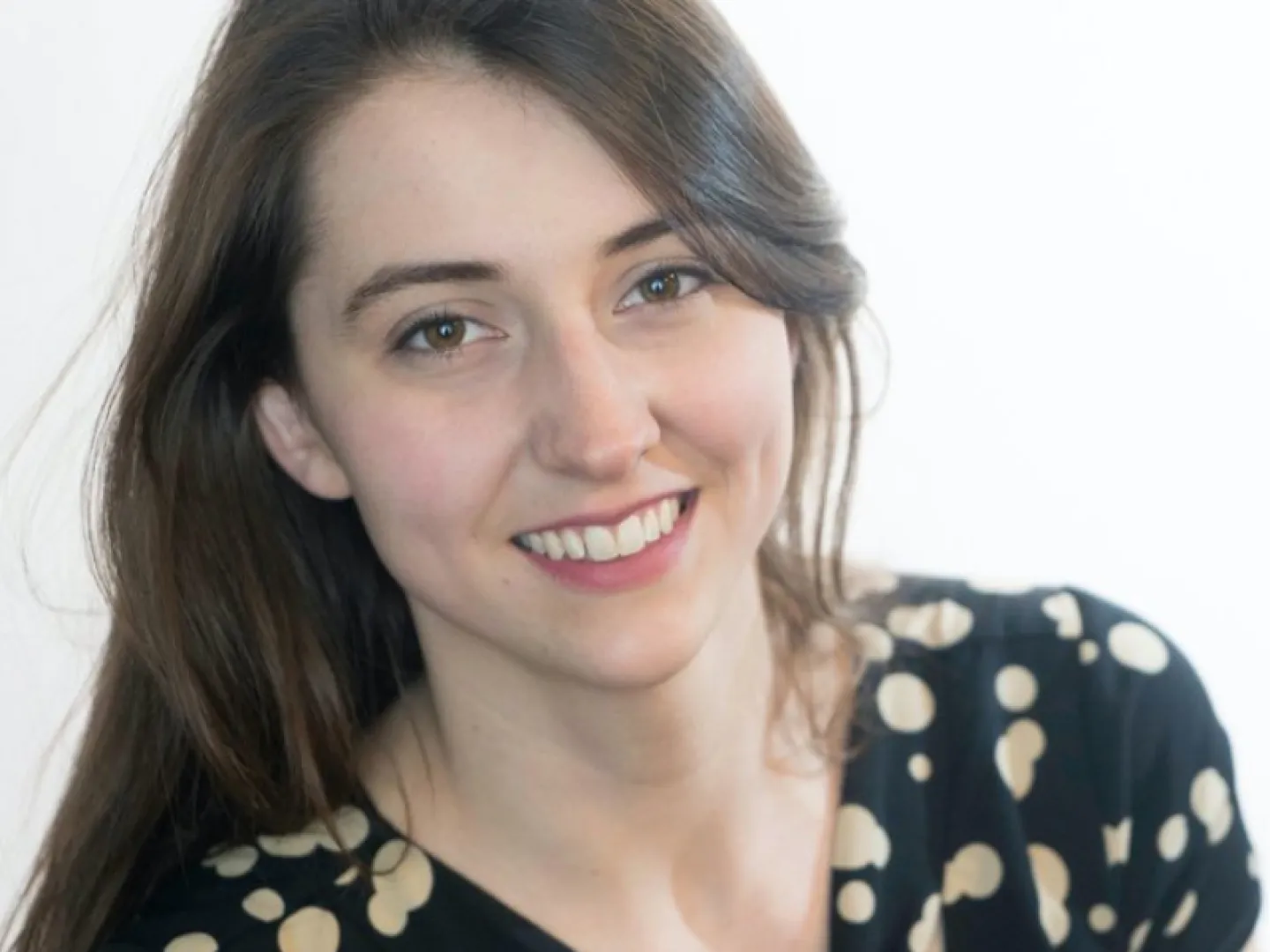 White woman with brown hair smiling wearing a polka dot shirt
