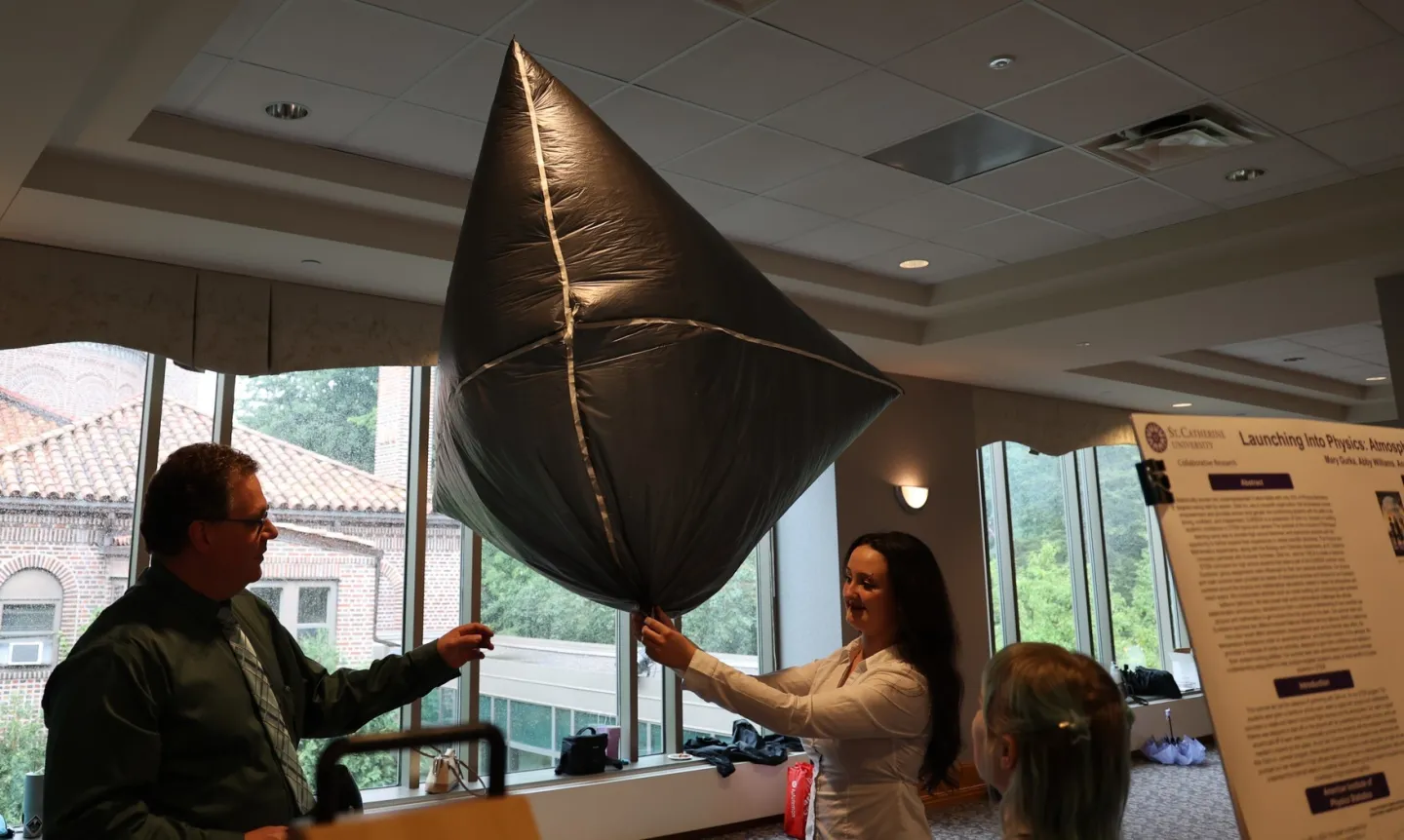 A student and a professor hold up a silver balloon used for atmospheric research.