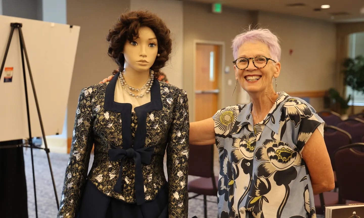 A professor stands next to a mannequin wearing a dress created by her team.