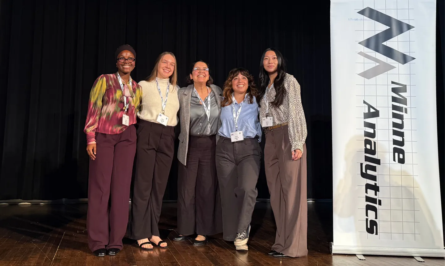 A group of four St. Kate's students and their supervisor gather on stage to celebrate a team win at the student data challenge by MinneAnalytics.